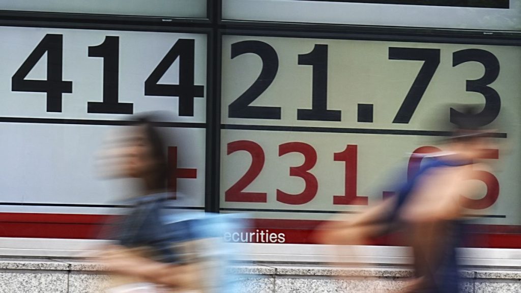 People walk in front of an electronic stock board showing Japan