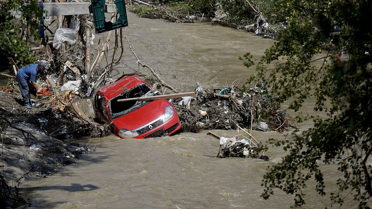 A man uses a chainsaw to cut tree stumps to free a washed up car carried downstream by the recent flash flood in Arges, 30 July, 2024