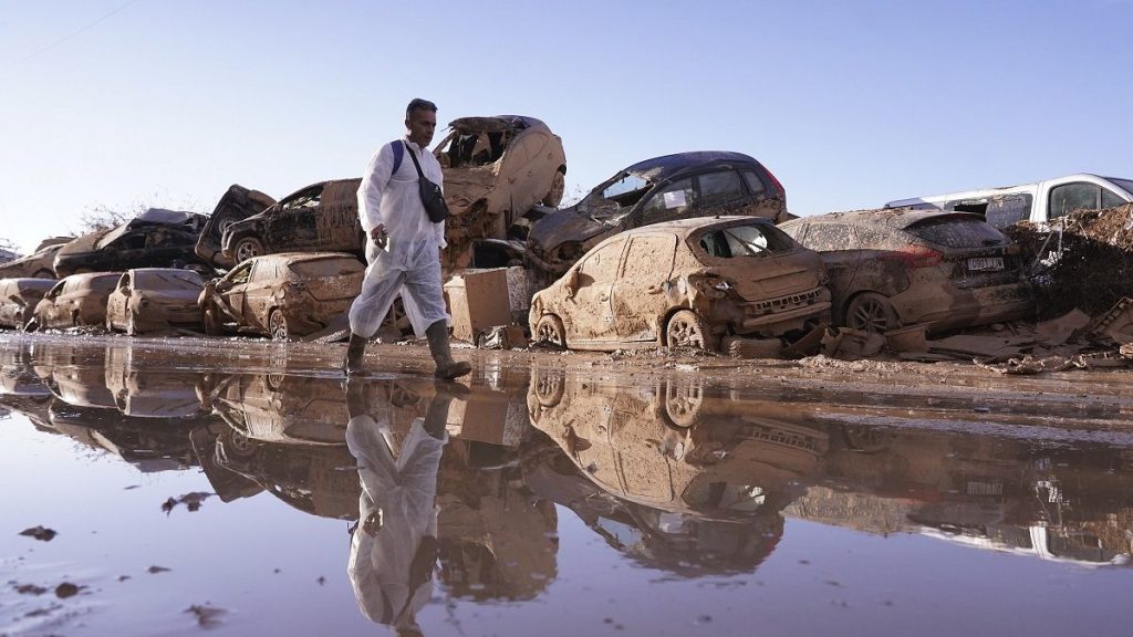 A man walks past stacked up cars after floods in Catarroja that left hundreds dead or missing in the Valencia region in Spain, Tuesday, Nov. 12, 2024.