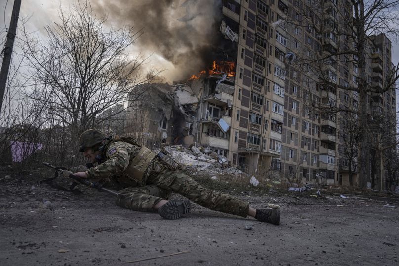 Un policier ukrainien se met à couvert devant un bâtiment en feu qui a été touché lors d'une frappe aérienne russe à Avdiivka, mars 2023.
