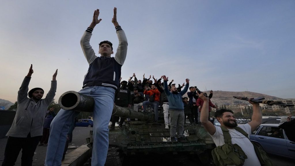 Syrian citizens stand on a government forces tank, that was left on a street, as they are celebrating during the second day of the take over of the city by the insurgents.