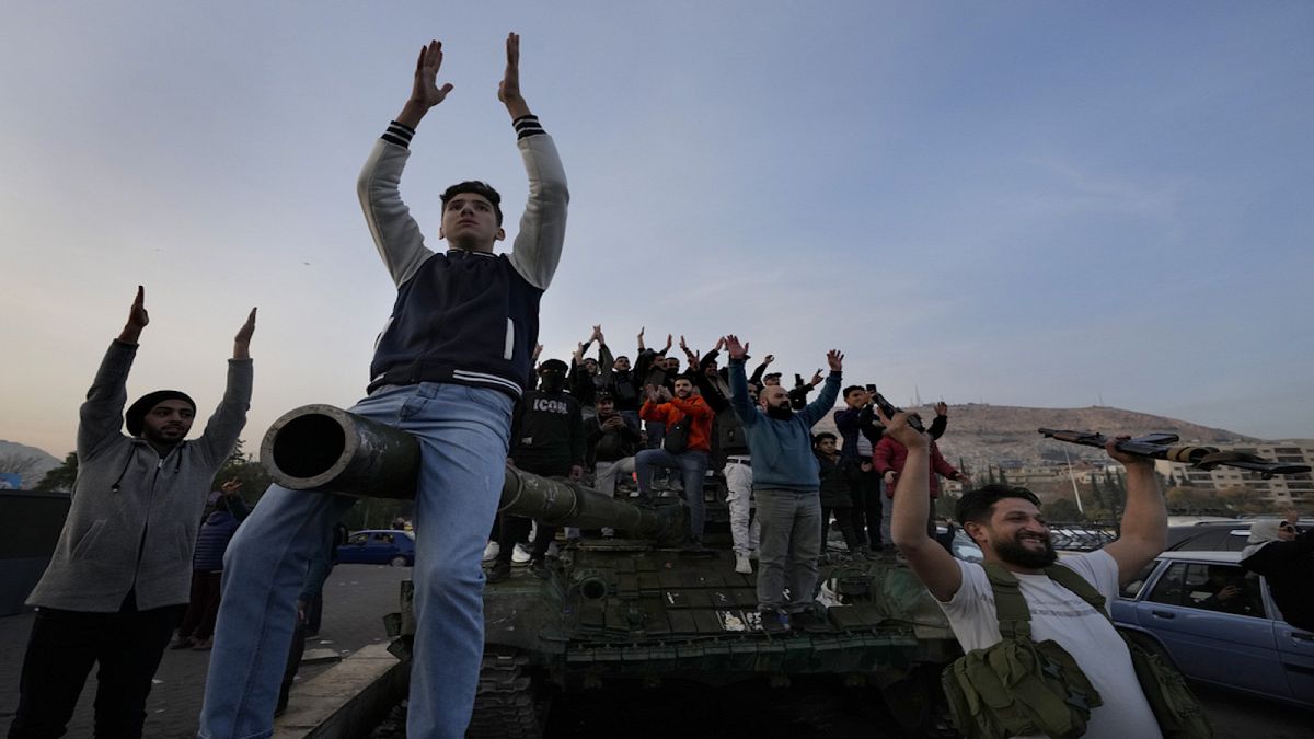 Syrian citizens stand on a government forces tank, that was left on a street, as they are celebrating during the second day of the take over of the city by the insurgents.