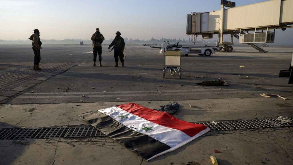 A Syrian flag lies on the ground as opposition fighters stand on the tarmac of the Aleppo international airport, Monday, Dec. 2, 2024.