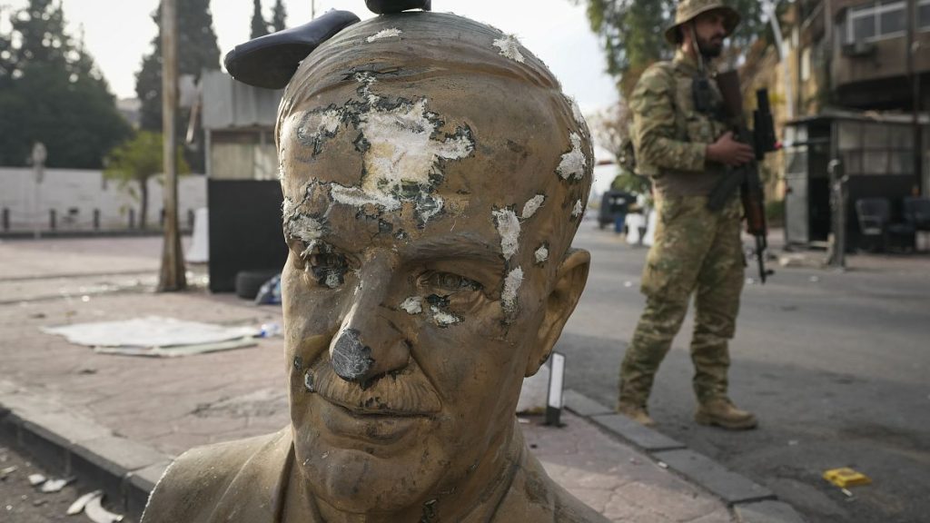 An opposition fighter in military uniform stands next to a broken bust of the late Syrian President Hafez Assad in Damascus.