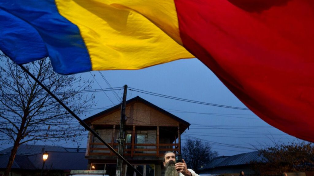 A man waves the Romanian flag outside the closed voting station in Mogosoaia, Romania, Sunday, Dec. 8, 2024.