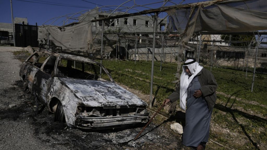 A Palestinian stands beside a torched car in the aftermath of an attack by suspected Israeli settlers in the West Bank village