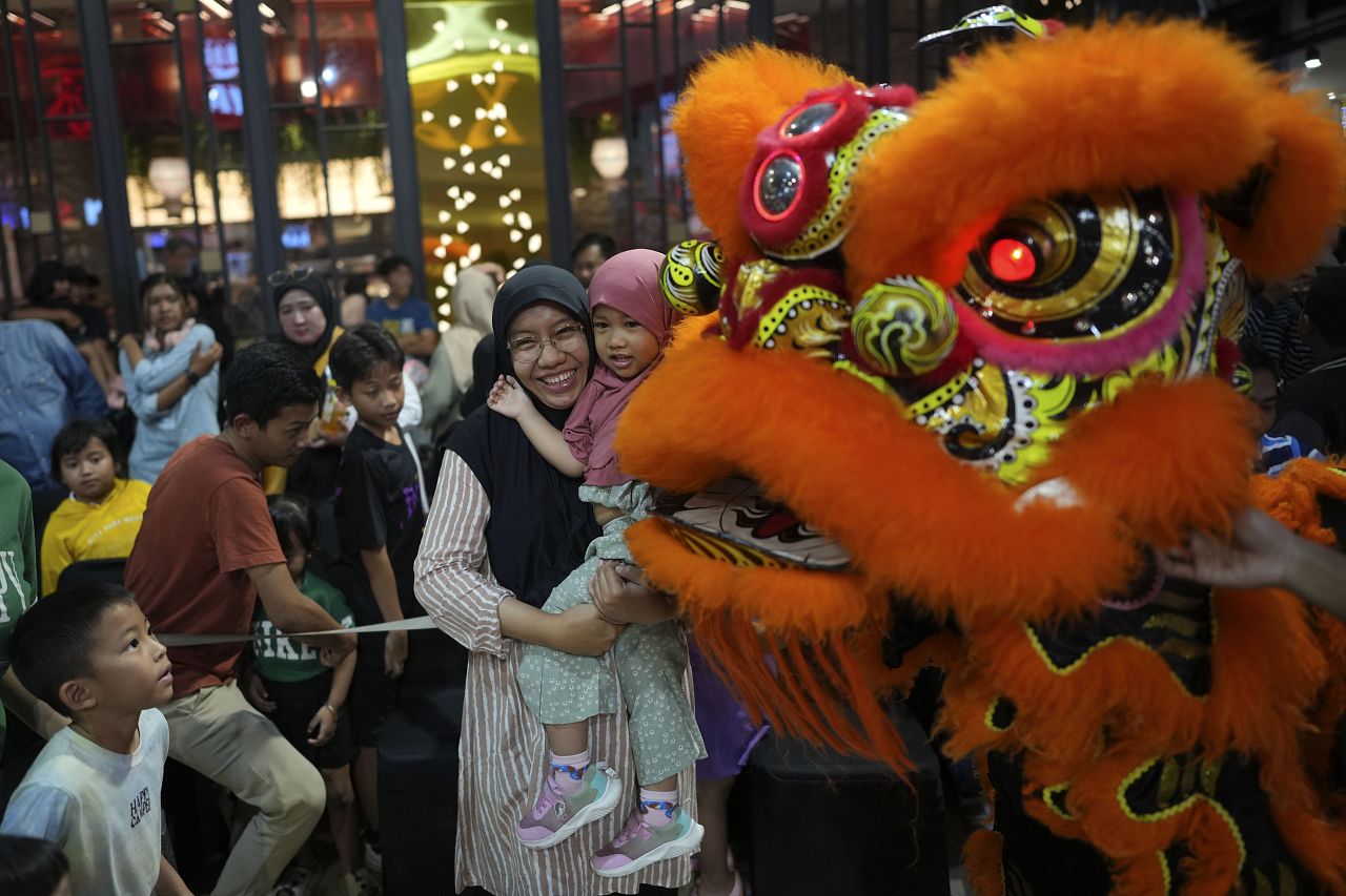 Une femme musulmane et sa fille ont leur photo prise avec des membres du club de danse du dragon Naga Merah Putih (dragon blanc rouge)