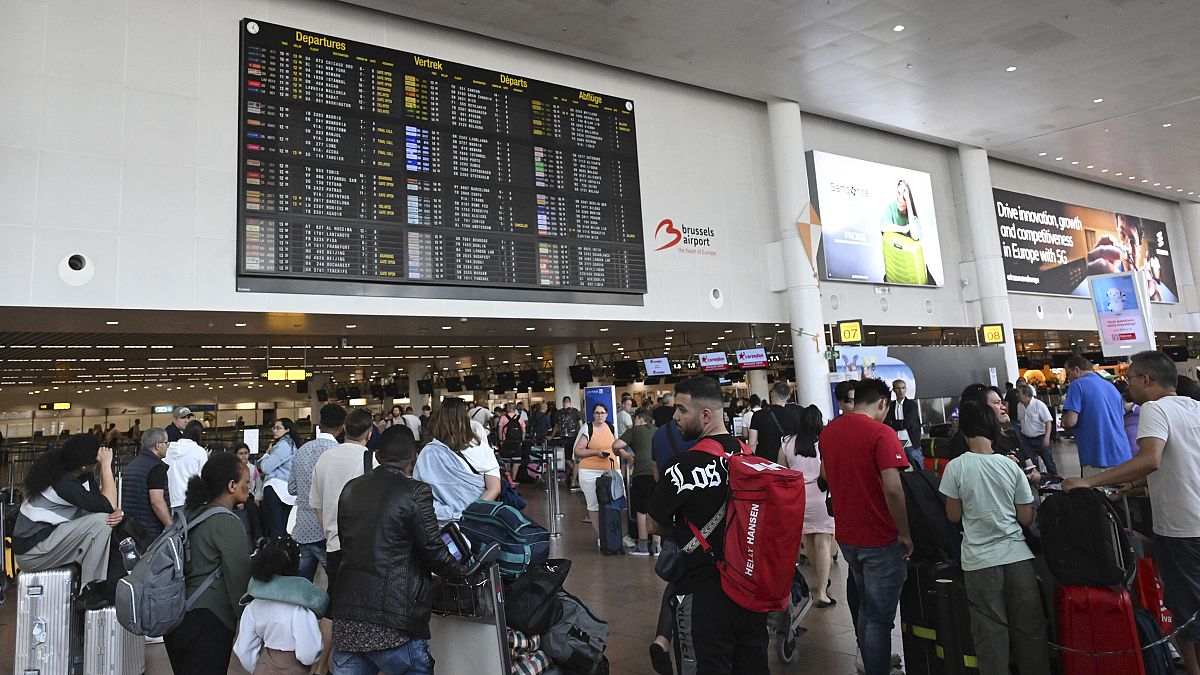 Travelers wait for information in front of a departure board at Brussels International Airport in Brussels, 19 July, 2024