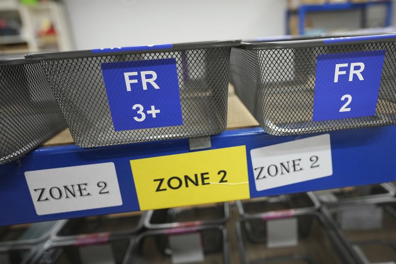 Des paniers montrant les codes de pays et les désignations d'étiquettes attendent le paquet des étiquettes des écoliers à l'usine «My Nametags» à Londres, le jeudi 30 janvier 2025.