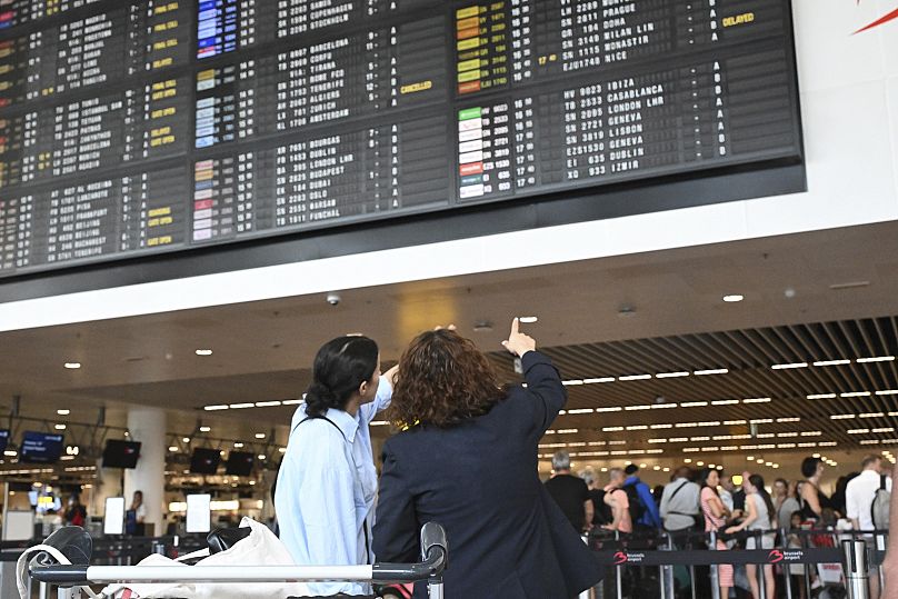Les voyageurs attendent des informations devant une planche de départ à l'aéroport international de Bruxelles à Bruxelles, 19 juillet 2024