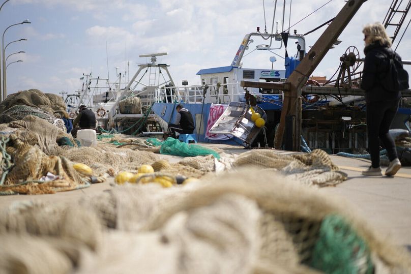 Les pêcheurs réparent des filets devant les bateaux de pêche au port dans le port romain de Fiumicino.