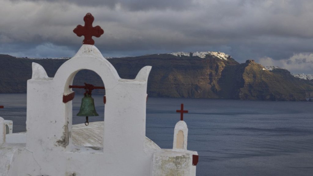 An Orthodox church in the town of Oia in Santorini, Greece, as the main town of Fira is lit by the sun in the background on 4 February 2025.
