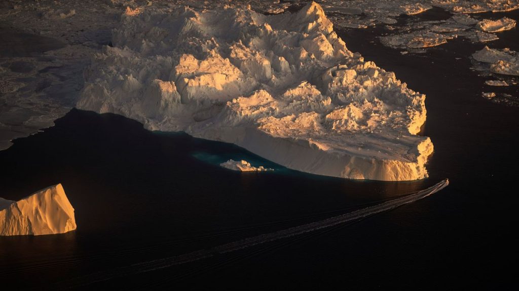 A ship sails alongside a large iceberg in Ilulissat, Greenland.