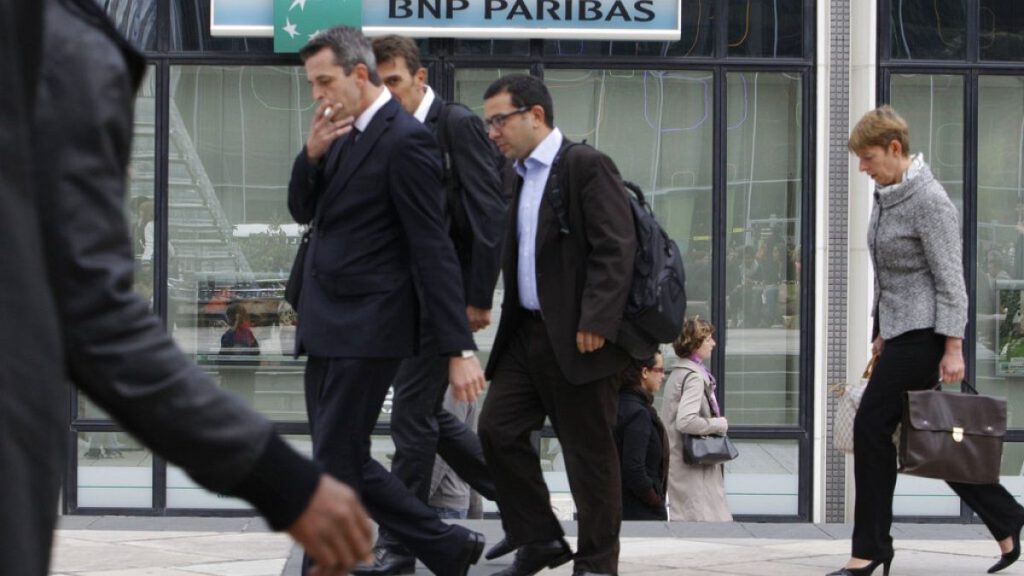 People walk past a logo of the BNP Paribas Bank at Paris business district La Defense, Tuesday, Sept. 20, 2011.