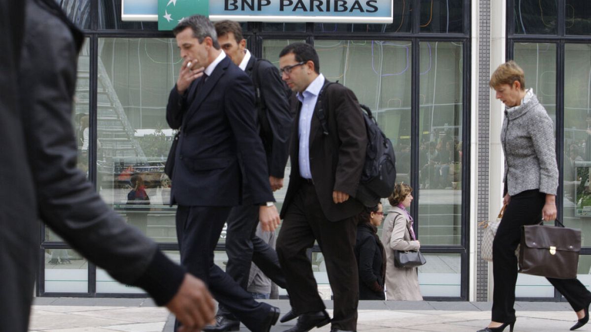 People walk past a logo of the BNP Paribas Bank at Paris business district La Defense, Tuesday, Sept. 20, 2011.