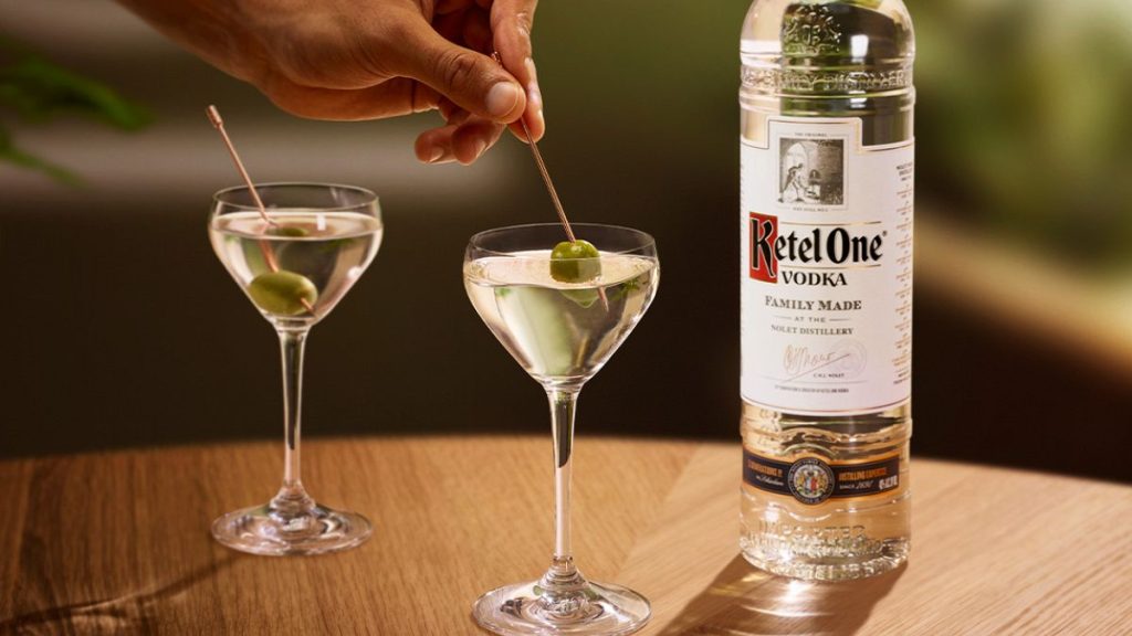 A bottle of Ketel One vodka and two dirty martinis on a table.