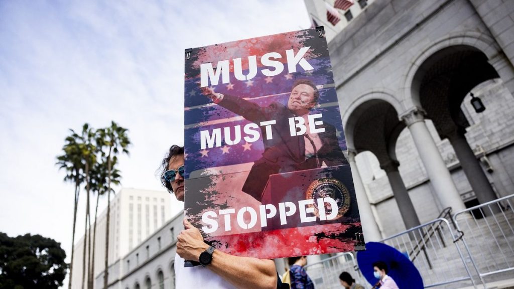 A demonstrator holds a poster of Elon Musk during a rally to protest President Trump