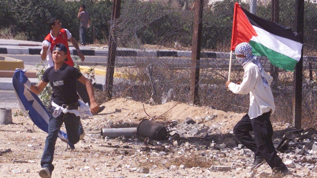 FILE - Man waves a Palestinian flag at the Netzarim Jewish settlement crossing in southern Gaza during clashes with Israeli forces Monday Oct. 2, 2000.