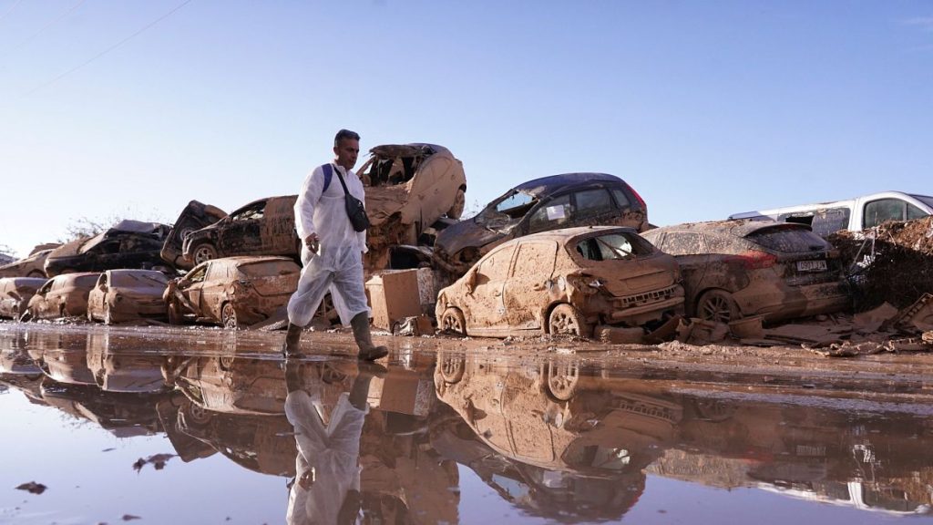 A man walks past stacked up cars after floods that left hundreds dead or missing in Spain