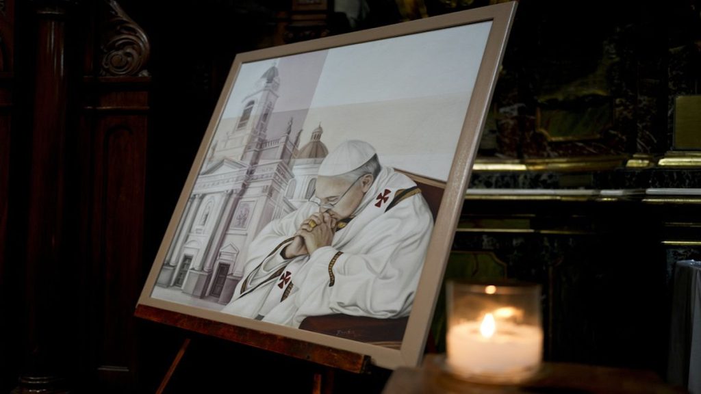 A candle glimmers alongside a painting of Pope Francis at San José de Flores basilica, Buenos Aires, Argentina, where he worshipped as a youth, Sunday, Feb. 23, 2025.