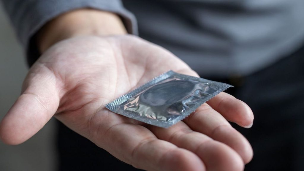 A man holds out a condom.