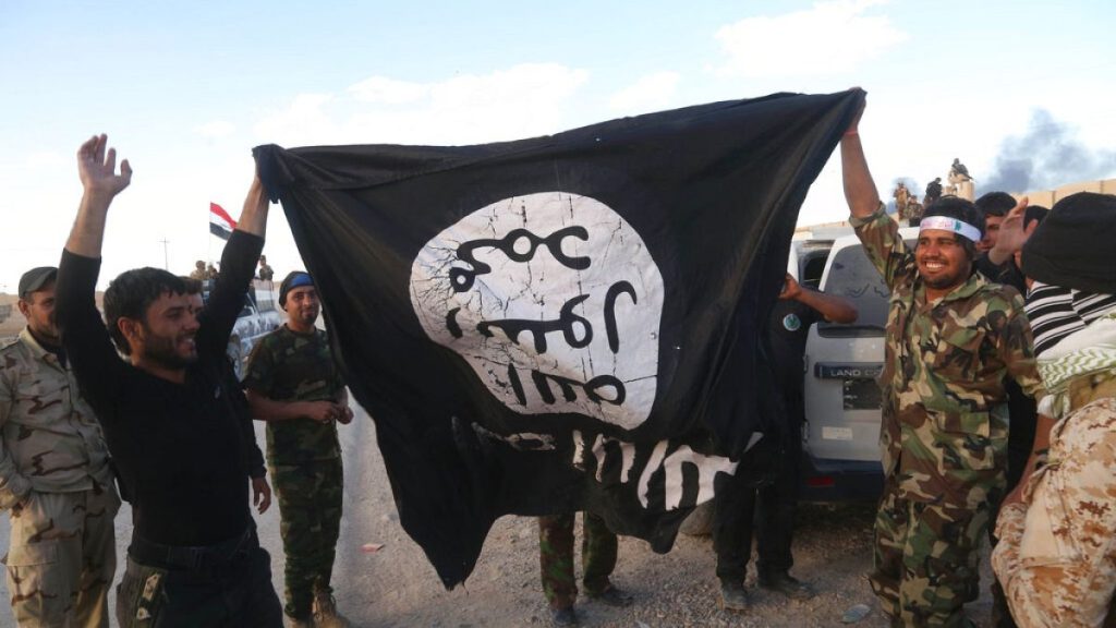 In this Tuesday, March 31, 2015 file photo, Iraqi security forces and allied Shiite militiamen celebrate as they hold a flag of the Islamic State.
