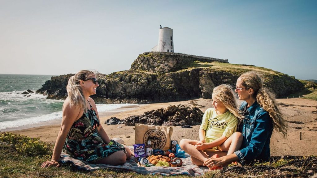 A young family on the beach with a lighthouse in the background, Isle of Anglesey, Wales
