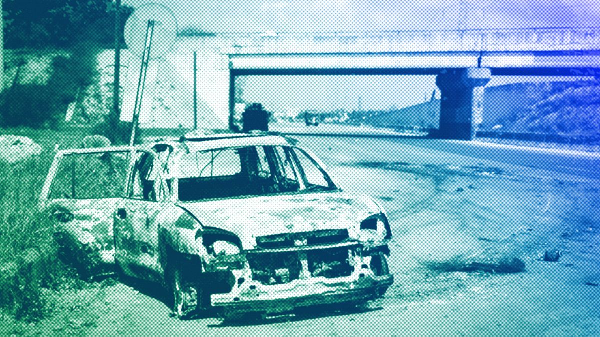 A burnt car remains in the middle of a empty road in the outskirts of the village of Qardaha, March 2025