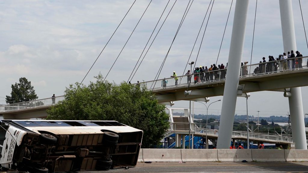 Pedestrians standing on a bridge look at a bus that overturned on a highway in Johannesburg, South Africa, on 11 March, 2025.