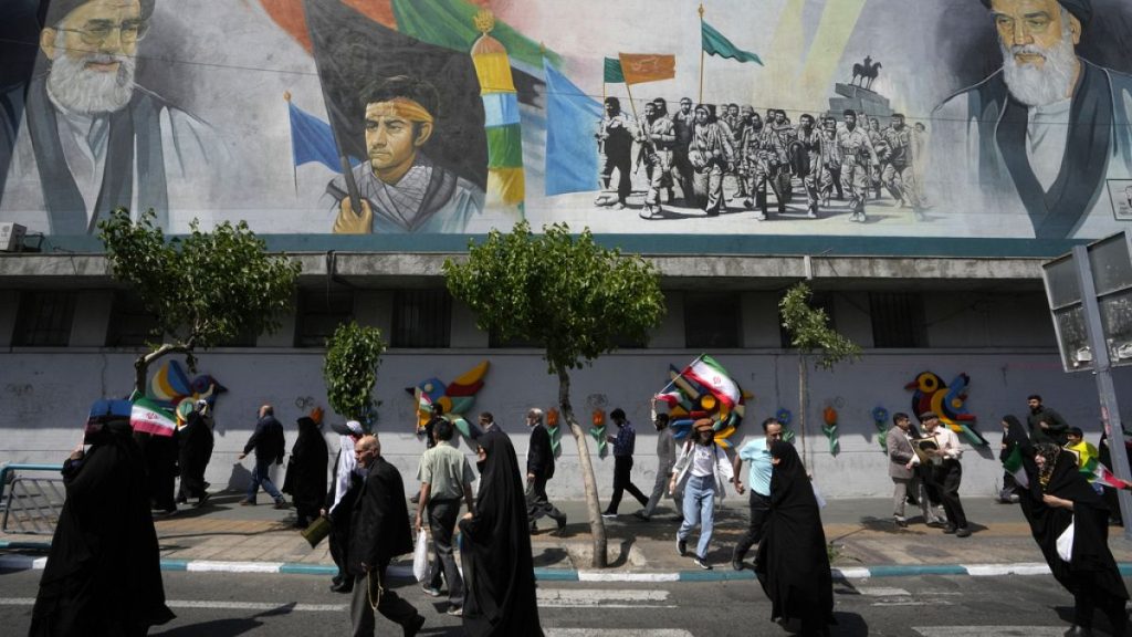 Iranian worshippers walk past a mural showing the late revolutionary founder Ayatollah Khomeini, right, Supreme Leader Ayatollah Ali Khamenei, left, and Basij paramilitary for
