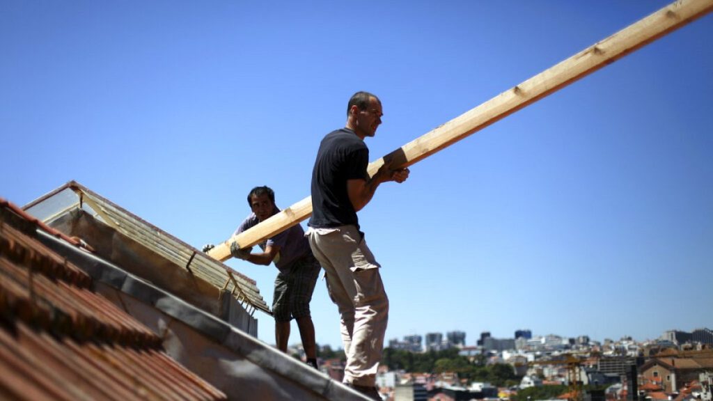 onstruction workers stand on the roof of a building in downtown Lisbon, Friday, Aug. 9, 2013.