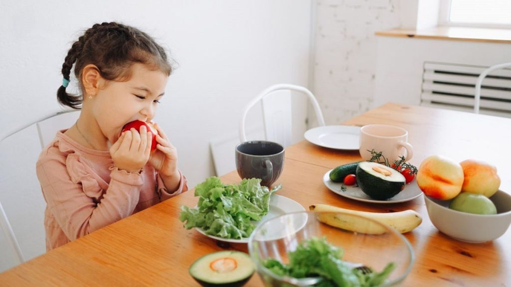 A little girl eats a fruit.