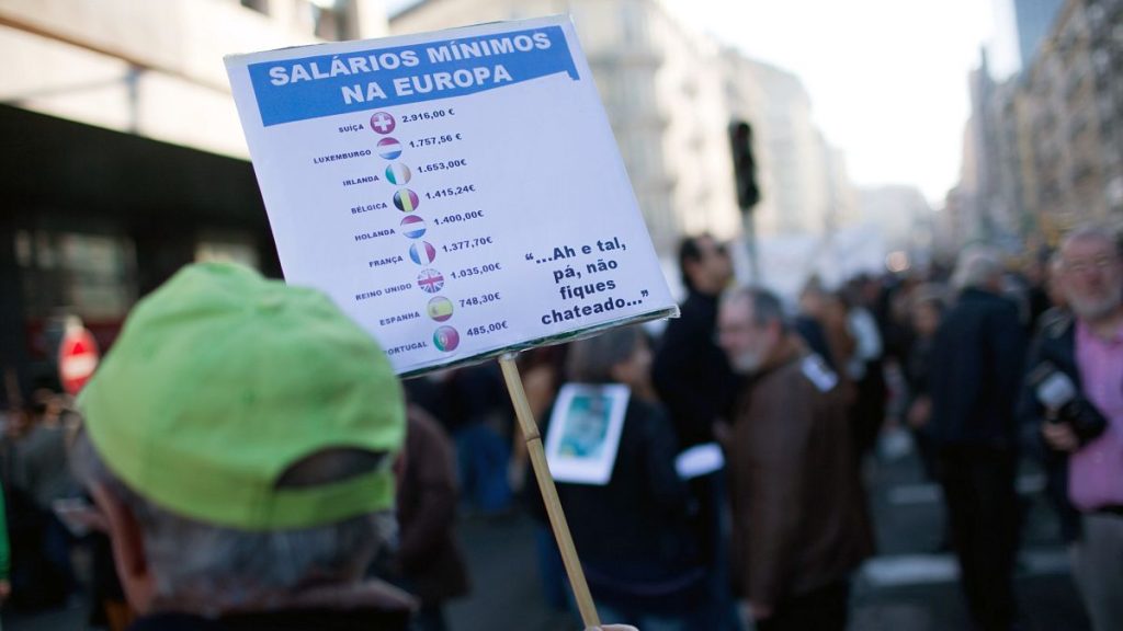 A man holds a sign with the minimum wage of different European countries during a protest against the government