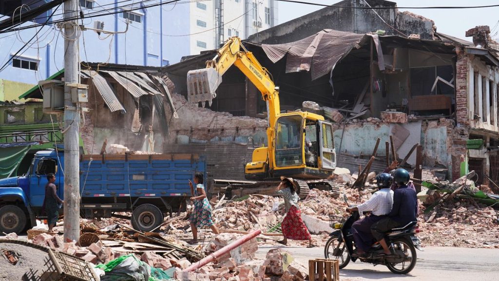 Local residents ride motorbikes while rescuers clean debris from damaged buildings in the aftermath of Friday