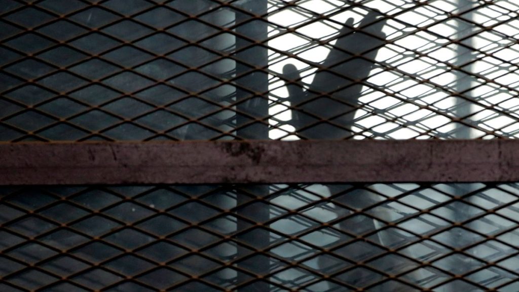 In this Aug. 22, 2015, file photo, a member of the Muslim Brotherhood waves his hand from a defendants cage in a courtroom in Torah prison, southern Cairo, Egypt.
