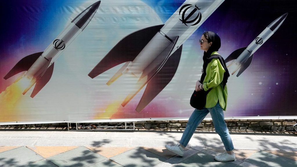 A woman walks past a banner showing missiles being launched, in northern Tehran, Iran.