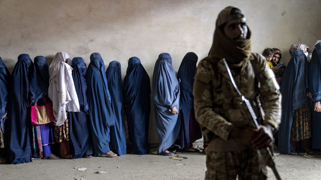 A Taliban fighter stands guard as women wait to receive food rations distributed by a humanitarian aid group in Kabul, 23 May, 2023