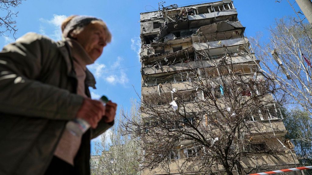 A woman walks in front of a multi-storey building damaged by a Russian strike on a residential neighbourhood in Zaporizhzhia, 22 April, 2025