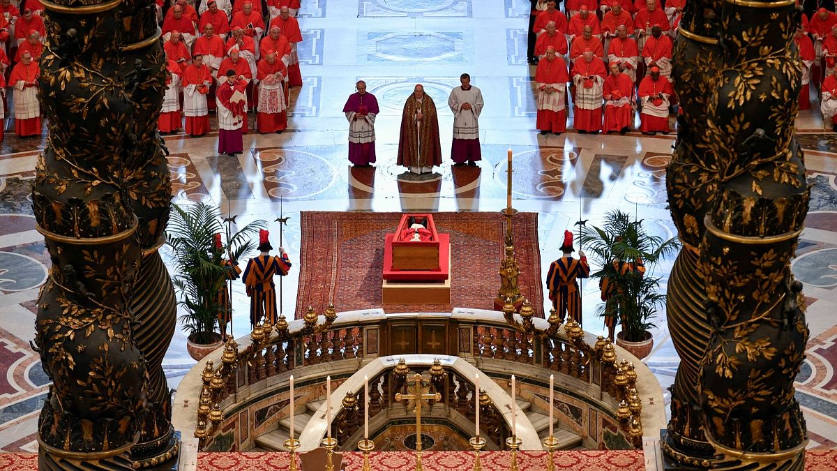 Cardinal Camerlengo Kevin Joseph Farrell and others pray in front of Pope Francis