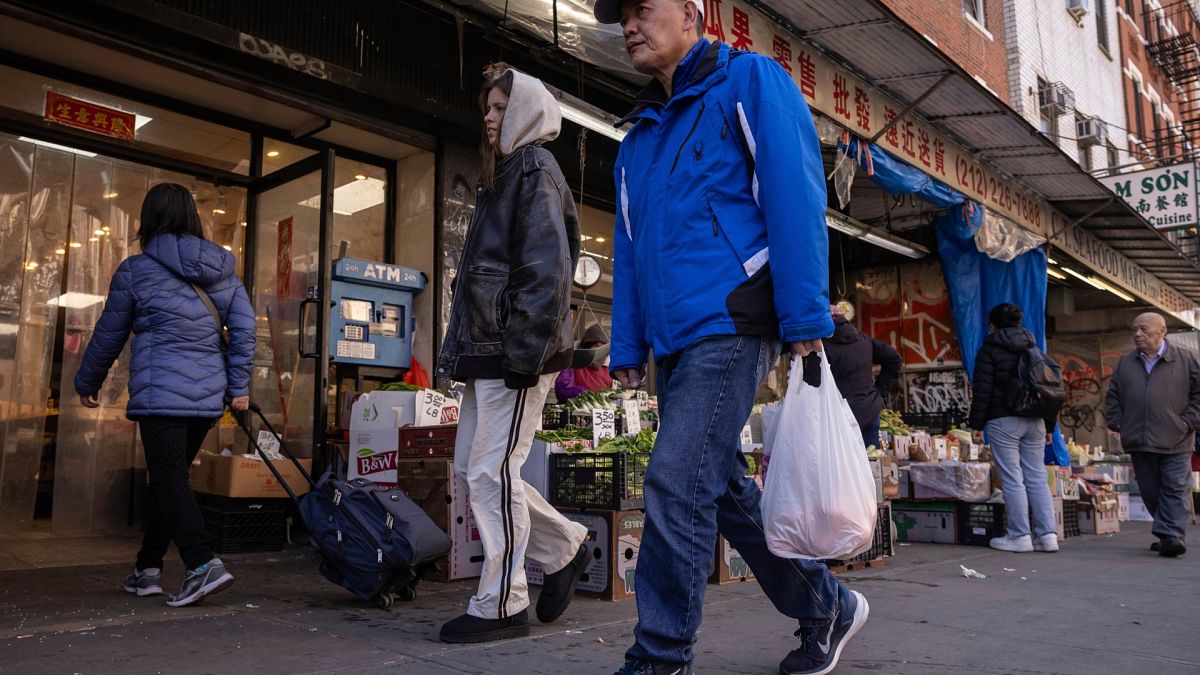 A person carrying a shopping bag walks past a grocery store in the Chinatown neighborhood, Wednesday, April 9, 2025, in New York.