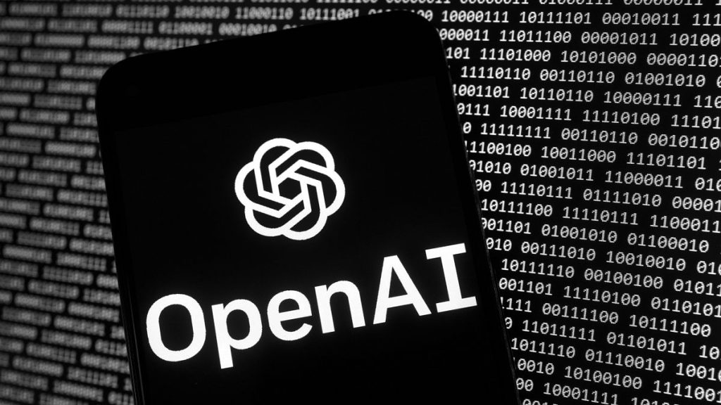 The OpenAI logo appears on a mobile phone in front of a computer screen with random binary data. 9 March 2023.