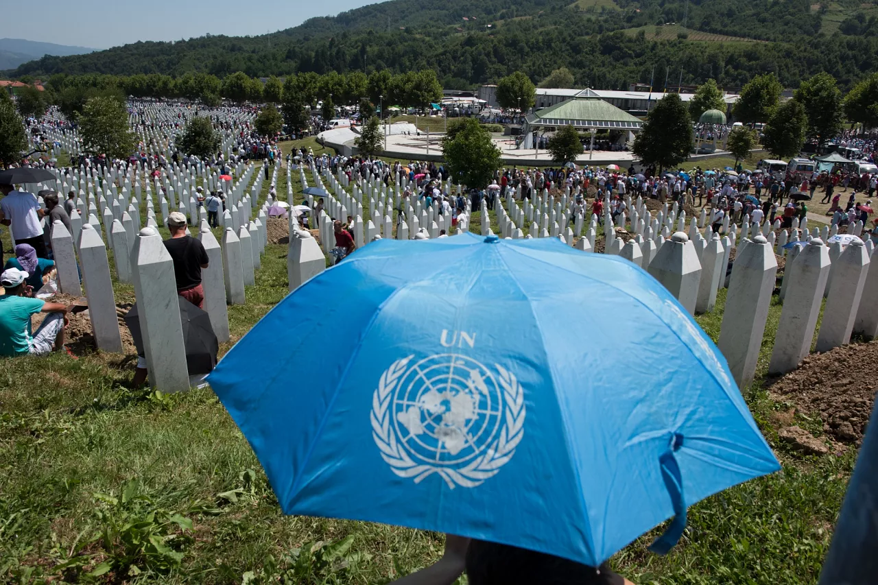Une personne tenant un parapluie bleu de l'ONU surplombe le mémorial de Srebrenica-Potočari