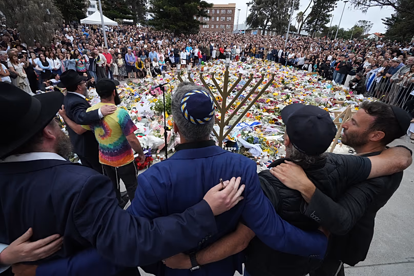 Les personnes en deuil se rassemblent lors d'une cérémonie d'allumage de la menorah à un mémorial floral pour les victimes de la fusillade de Bondi Beach, le 16 décembre 2025.