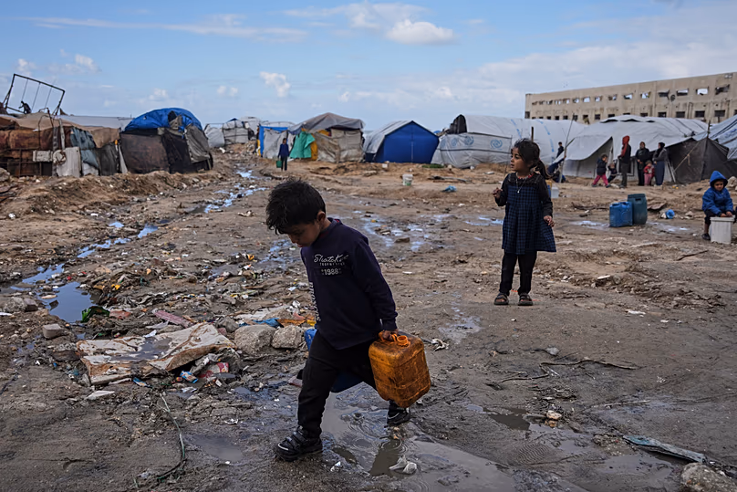 Des enfants palestiniens transportent des jerrycans en plastique remplis d'eau alors qu'ils traversent un camp de déplacés dans la ville de Gaza, le 28 décembre 2025.
