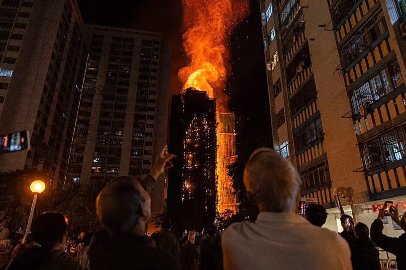 Des gens regardent les flammes engloutir un bâtiment après qu'un incendie se soit déclaré au tribunal de Wang Fuk à Hong Kong, le 26 novembre 2025.