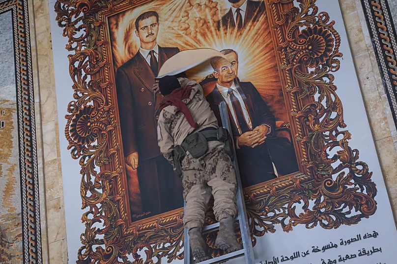 A Syrian opposition fighter tears a painting depicting Syria’s overthrown President Bashar al-Assad and his late father Hazef at Aleppo International Airport, 2 December, 2024