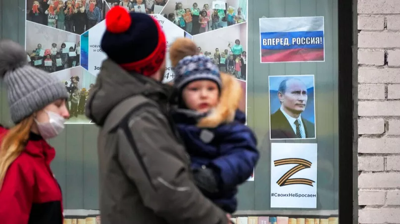 Une famille passe devant un portrait du président russe, une pancarte indiquant « Go Russia ! » et la lettre Z à Saint-Pétersbourg