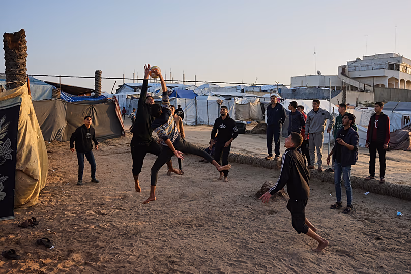 De jeunes Palestiniens jouent au volley-ball dans un camp de tentes abritant des familles déplacées à Deir al-Balah, dans le centre de la bande de Gaza, le mardi 20 janvier 2026.