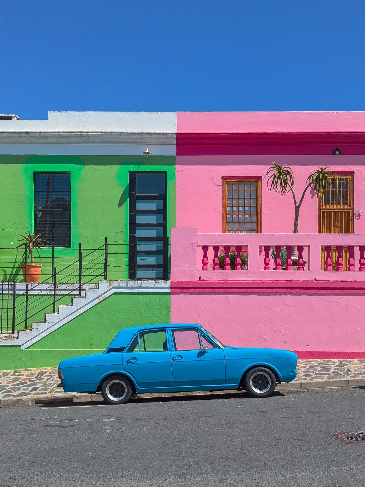 Color Divides représente la juxtaposition d'une voiture bleue avec des bâtiments vert vif et roses du quartier de Bo-Kaap, à Cape Town, en Afrique du Sud.