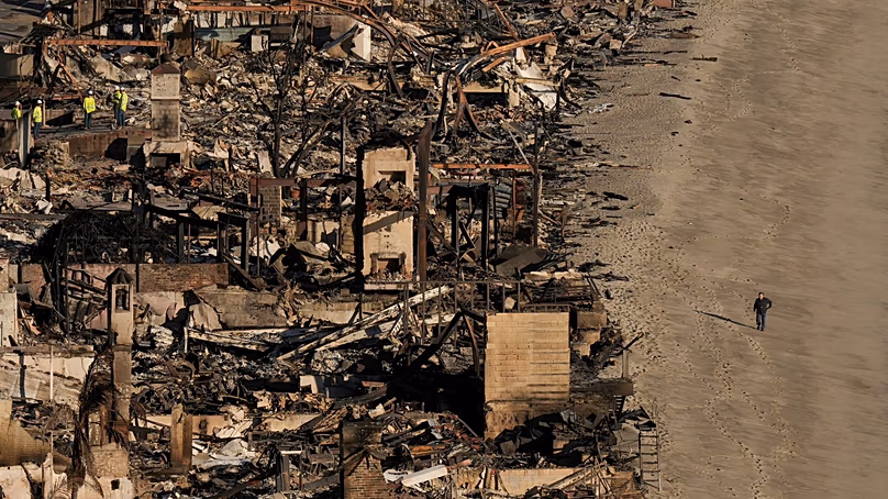 DOSSIER - Une personne marche sur la plage à côté de maisons endommagées par l'incendie des Palisades, le 16 janvier 2025, à Malibu, en Californie.